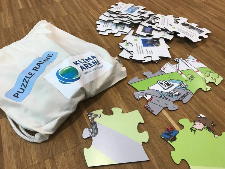 Auf dem Tisch liegen zahlreiche bunte Puzzleteile neben einem Beutel mit der Aufschrift "Puzzle Rallye" der KLIMA ARENA.