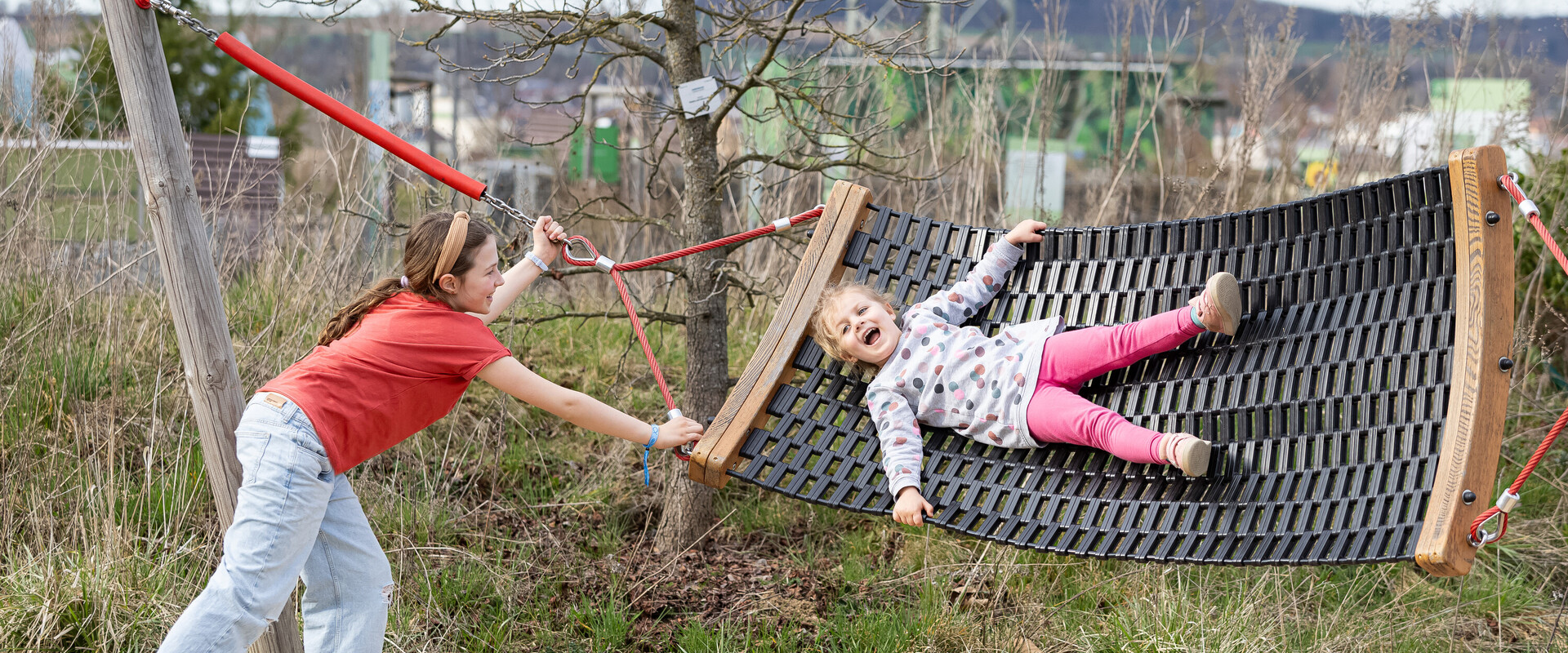 Ein M&auml;dchen liegt lachend in einer H&auml;ngematte, ein zweites M&auml;dchen bewegt die H&auml;ngematte.